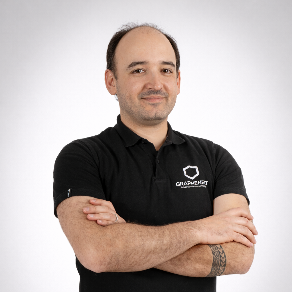 Smiling man with folded arms wearing a black polo with a logo on the chest, neutral studio background