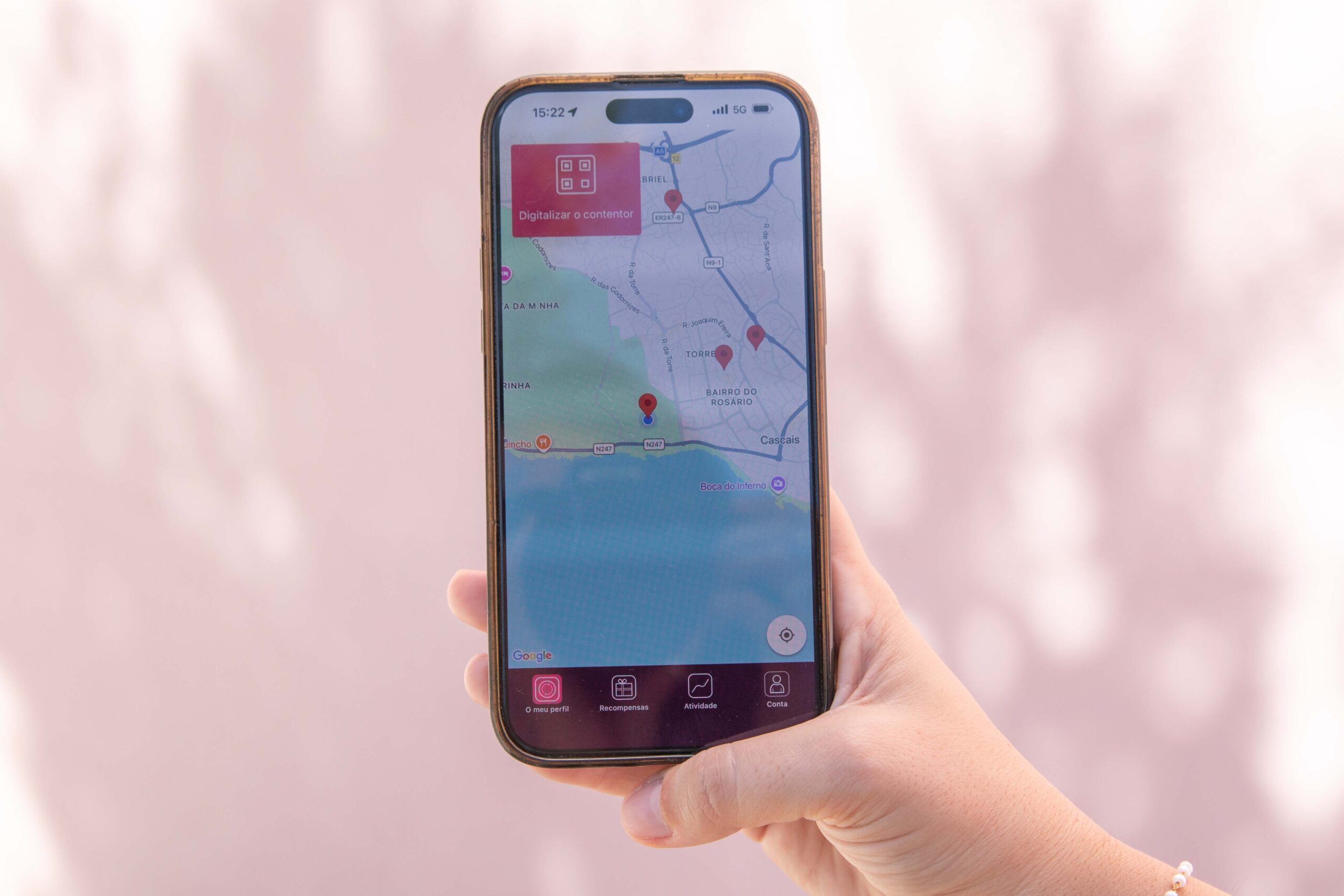 Person holding a smartphone showing a map app with red location pin and UI at the bottom (Portuguese labels visible).