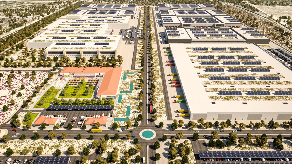 Aerial view of a solar-powered logistics campus with large warehouses, rooftop solar panels, loading docks, and a circular roundabout at a street intersection.