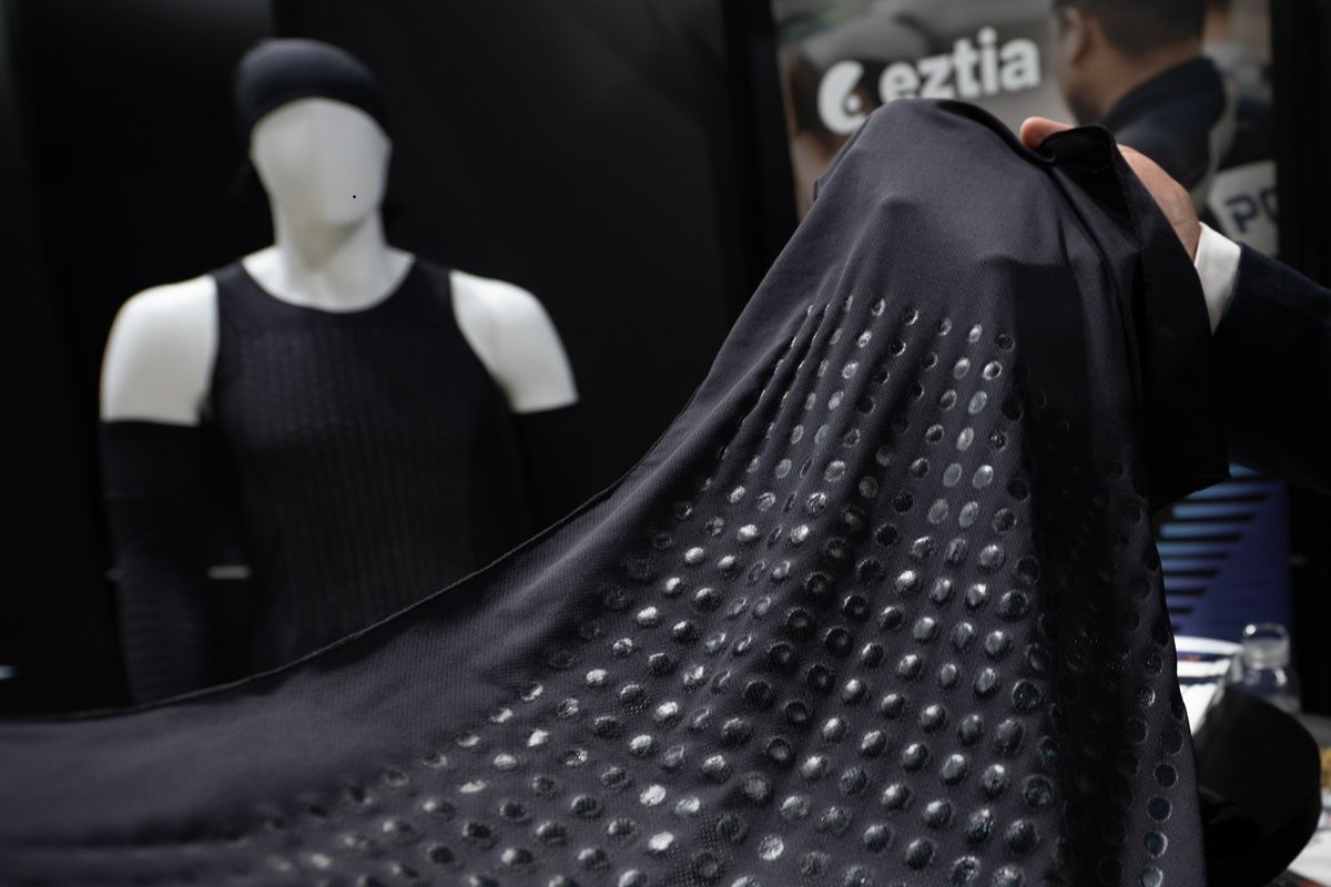 Close-up of a person handling a dark, dotted fabric in a fashion store, with a black-dressed mannequin in the background.